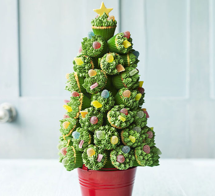 many cupcakes with green frosting, decorated with jelly candies, put in the shape of a christmas tree with red bucket on bottom and yellow star on top