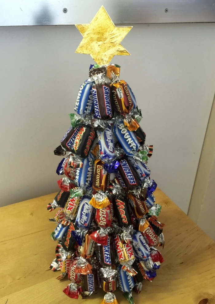 christmas tree made of miniature candy bars, with a six pointed paper star in gold, placed on wooden desk with light background