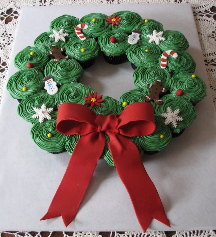 batch of cupcakes with green icing, decorated with festive fondant shapes, put in the form of a christmas wreath, decorated with big red fondant bow