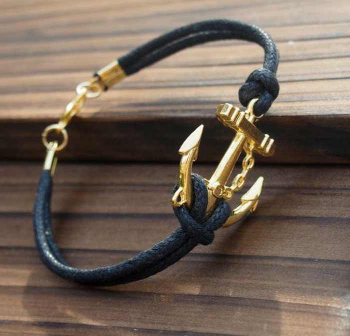 black woven leather bracelet with golden closure, featuring a golden anchor detail tied with knots, on wooden surface