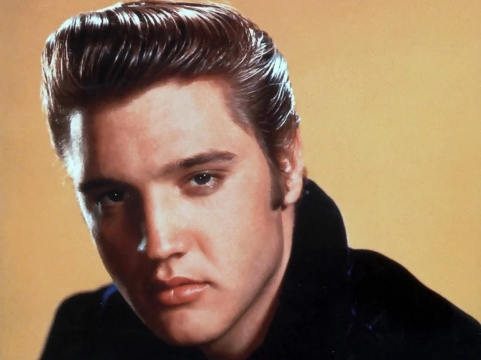 color photo of elvis presley, gelled up shiny dark hair, black top and yellow background, close up with shadows on face