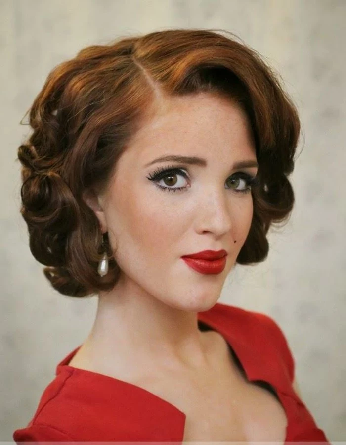 ginger-haired woman with 1940's styled short hair with curls, red lipstick and top, beauty spot fake lashes and mascara in close up