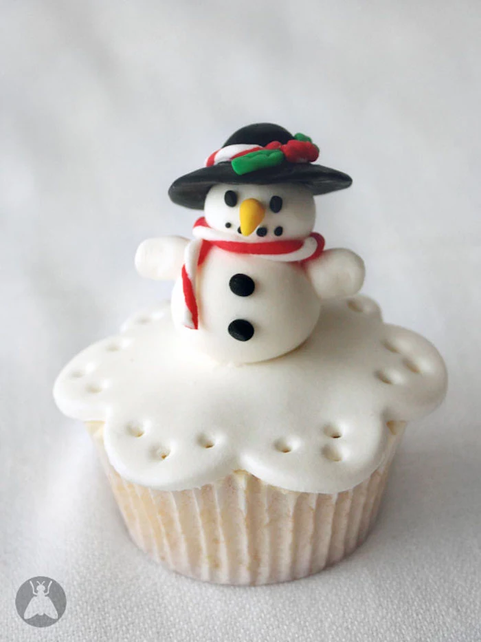 cupcake with white wrapper, and white fondant icing, decorated with snowman shape, wearing hat and scarf