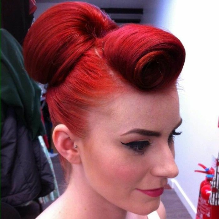 red-haired woman, with unusual curled bangs and a hair bun, wearing black eyeliner and fake lashes, dyed eyebrows and lipstick