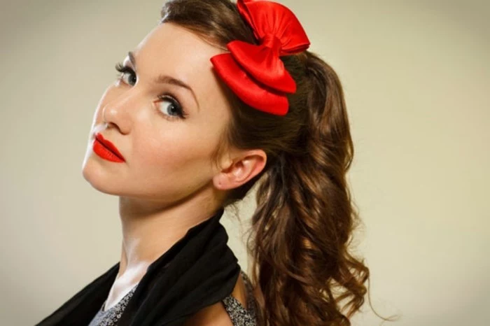 pin up hairstyles, close up of woman with retro side ponytail, two bright red bows and red lipstick, blue eyes fake eyelashes and a black scarf