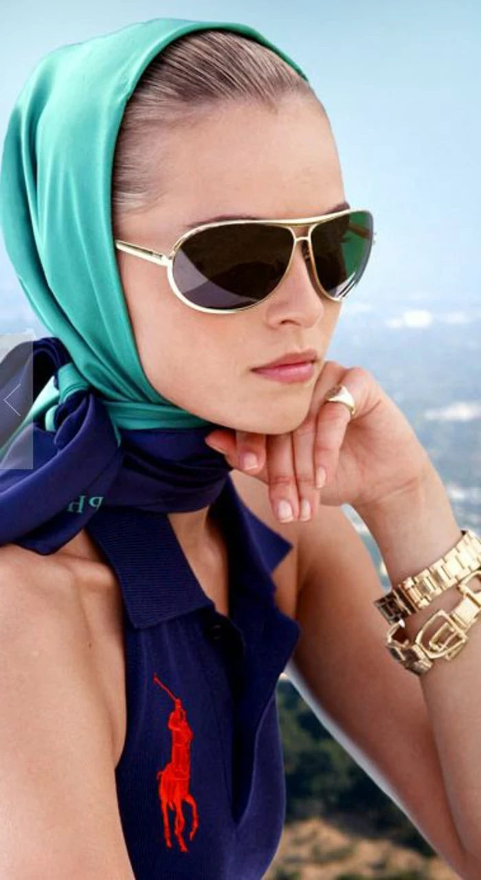 close up of woman with turquoise headscarf, wearing sunglasses and a blue sleeveless shirt with red big polo logo, golden wristwatch bracelet and ring 