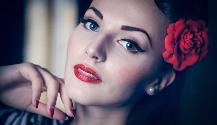 vintage hairstyles, close up of woman with heavy 1950's inspired make up, penciled eyebrows and fake red rose behind ear