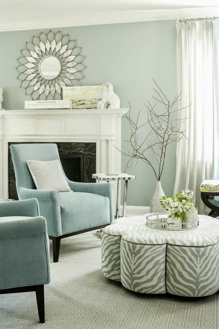 pale mint green room, two pale blue chairs, grey and white striped table, white fireplace and round ornate decorative mirror, white vase with dry branches