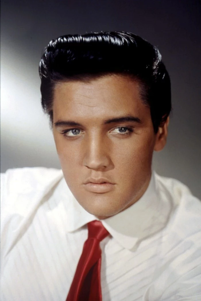 older elvis presley in colorized photo, shiny black gelled up hair, white shirt and shiny red tie, blue eyes and grey background