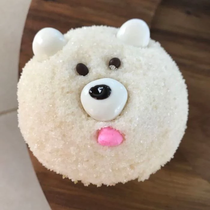 mini cupcake recipes, cupcake with white sparkly sugary icing, decorated with fondant and chocolate to look like polar bear, on a dark wooden table