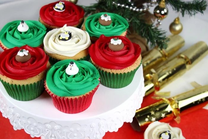 seven cupcakes on white dish, three with red frosting, three with green frosting, one with white frosting, decorated with festive fondant shapes
