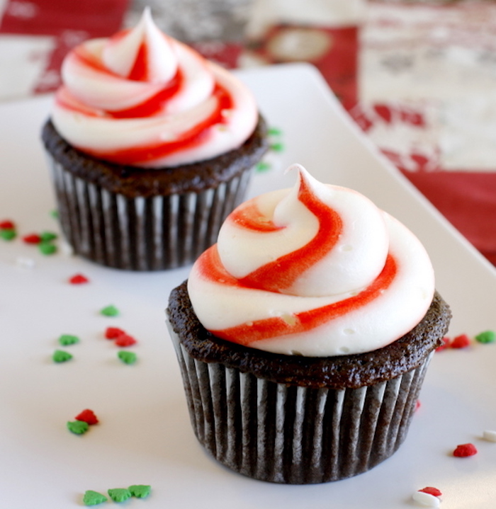 christmas flavors, two chocolate cupcakes on white plate with red and green sprinkles, with white and red swirly creamy icing