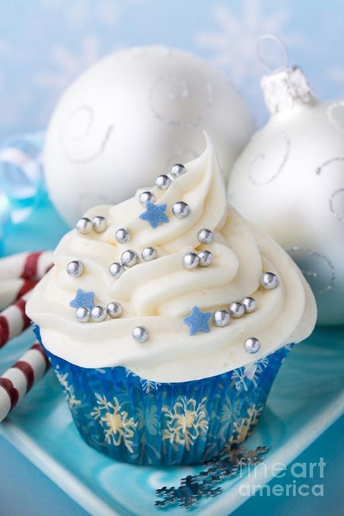 cupcake in blue wrapper, with white snowflake pattern, white icing decorated with small blue stars and silver pearls