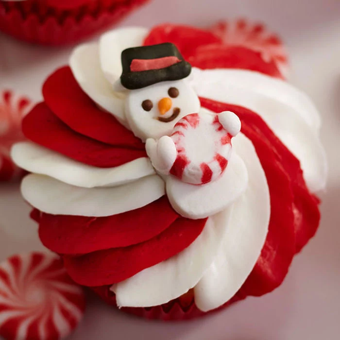 cupcake with white and red swirly icing, decorated with snowman fondant shape, holding peppermint candy