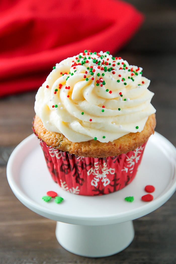 christmas baking ideas, yellow cupcake in red wrapper, with pale yellow creamy icing, decorated with red and green sprinkles