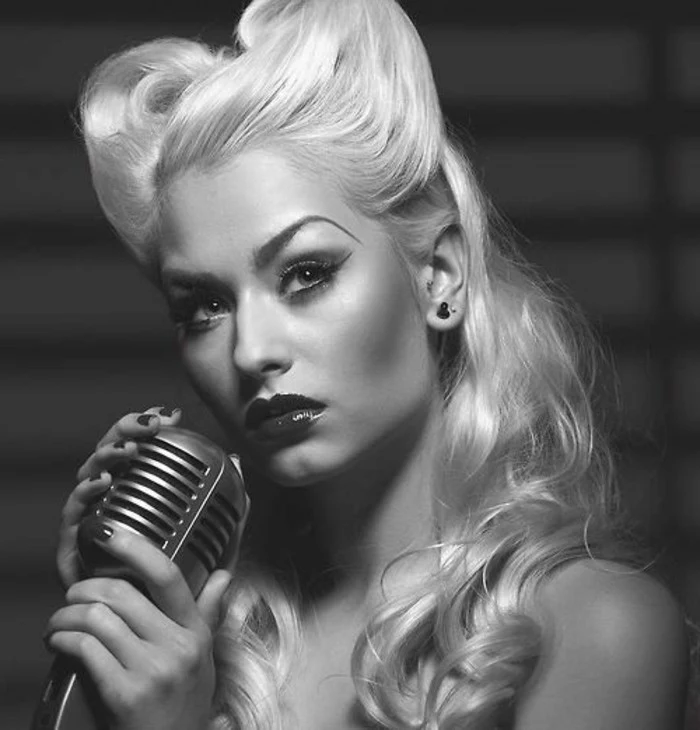 pinup hair, woman with light blonde hair and victory rolls, arched eyebrows heavy make up and dark shiny lipstick, holding a retro microphone