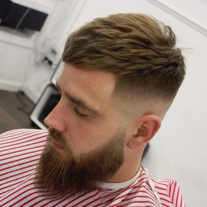 faded undercut, man with beard an mustache, facing down and to the side, hair shaven on the sides but gradually getting longer on top, red and white striped barber's robe