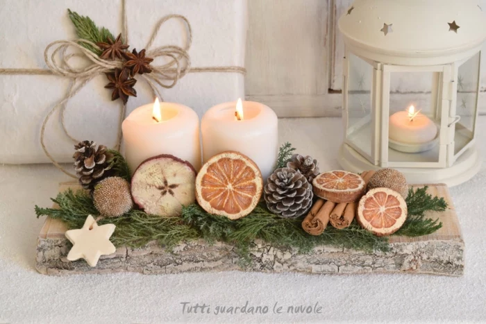 christmas crafts for adults, a chunky wooden board with two ccandles, decorated with pine cones cinnamon sticks a star-shaped cookie, with wooden circles painted like fruit slices, lantern and wrapped gift in background