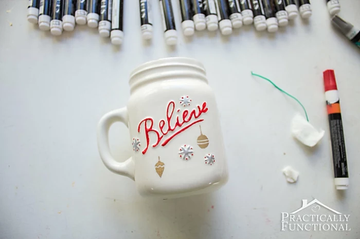 diy christmas crafts, red marker near white hand-painted mug, believe written in red and hand-painted details, markers in upper part of background, on white surface