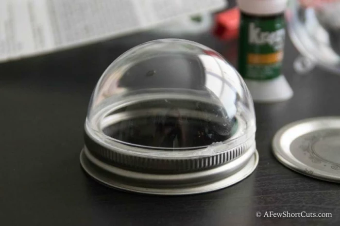 diy christmas gifts, plastic dome stuck on a ring-shaped jar lid, glue in the background