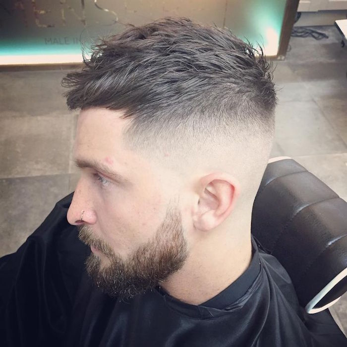 how to style a undercut, man with serious expression, with beard and mustache, hair trimmed very short on the side but kept longer and wavy on top, wearing black hairdresser's robe