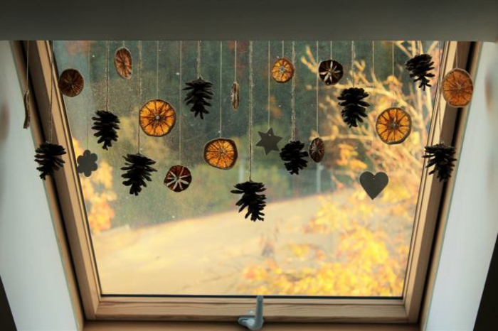 a window decorated with dried orange slices and pine cones, hanging on strings, with heart star and flower shapes