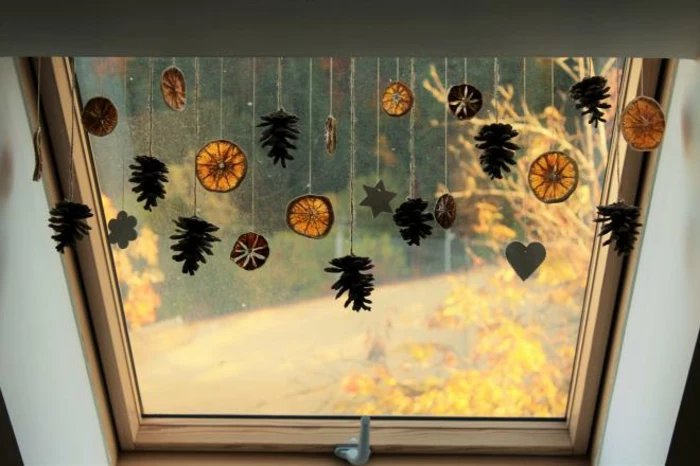 a window decorated with dried orange slices and pine cones, hanging on strings, with heart star and flower shapes