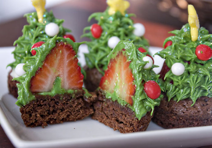 several chocolate brownies, with green frosting made to look like x-mas tree, decorated with white and red candies and little yellow stars, one brownie cut in half to reveal strawberry in icing