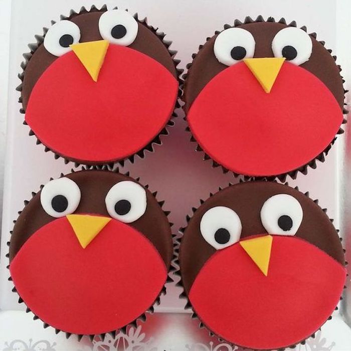 four cupcakes decorated with red and brown fondant, with yellow white and black details, made to look like birds 
