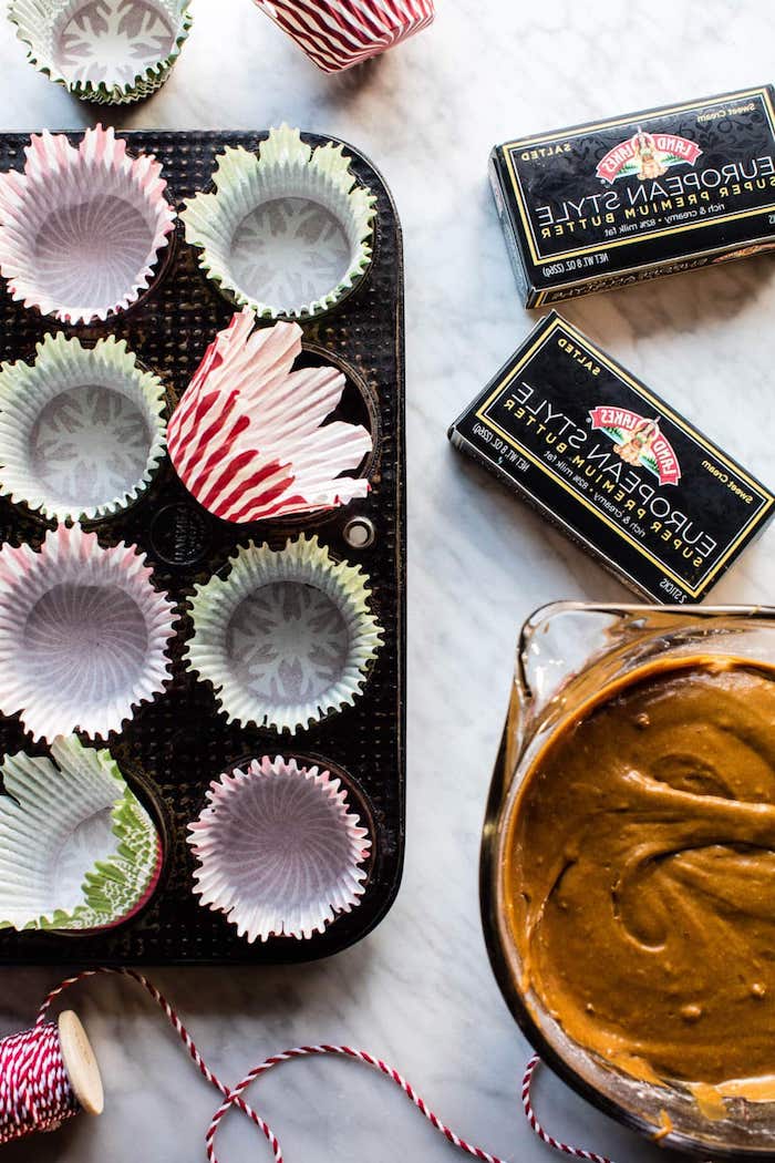 christmas cupcakes, cupcake mould lined with empty green and red wrappers, two packed sticks of butter, a bowl with brown mix, white and read thread