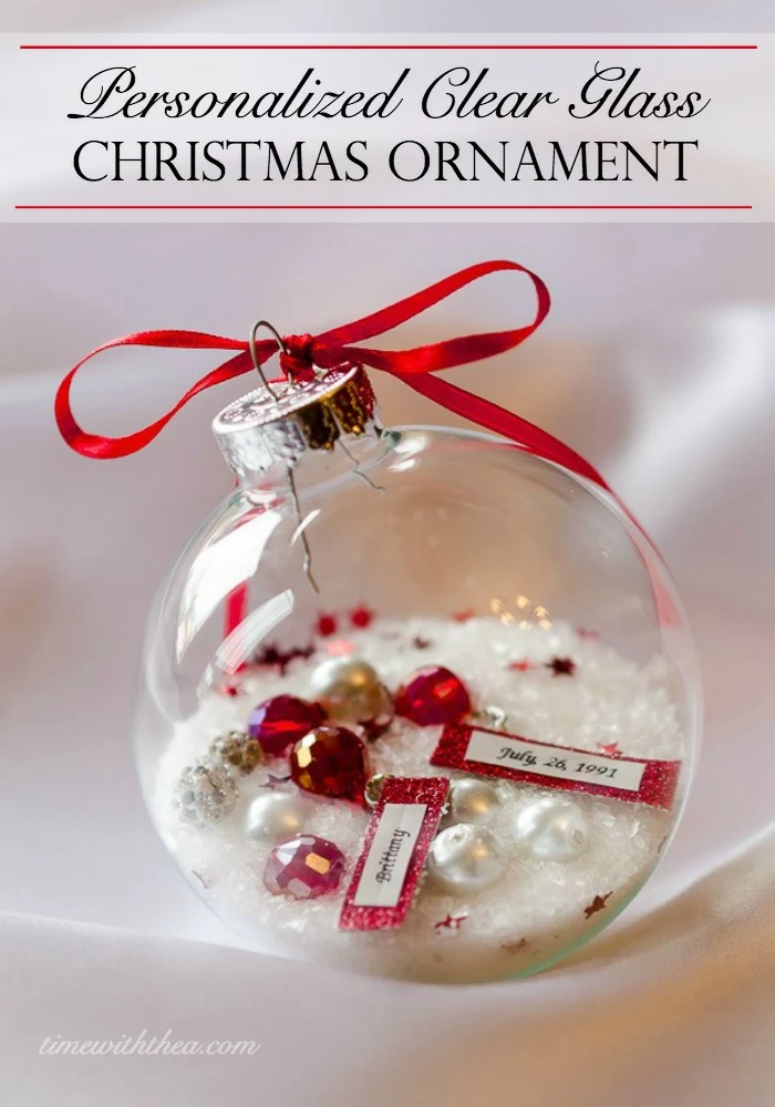 cheap christmas gift ideas, clear glass christmas bauble, filled with white glitter, fake pearls and red jewels, and pieces of paper with writing, silver cap tied with a red ribbon