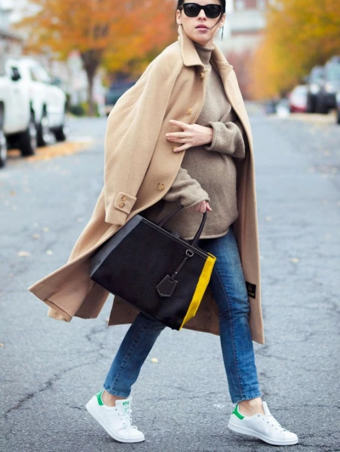 soft and long camel brown coat, worn by mother-to-be with blue jeans and large mink-colored sweater, sunglasses and black bag with yellow stripe, white sneakers with green details