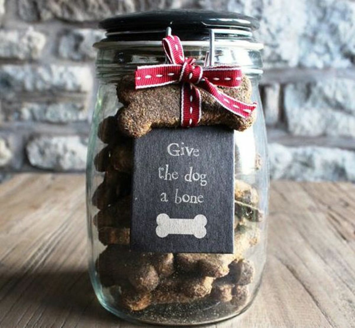 christmas crafts for adults, a clear jar with snap closure and black lid, containing homemade dog biscuits shaped like bones, one bone biscuit tied to closure with red and white ribbon, black label