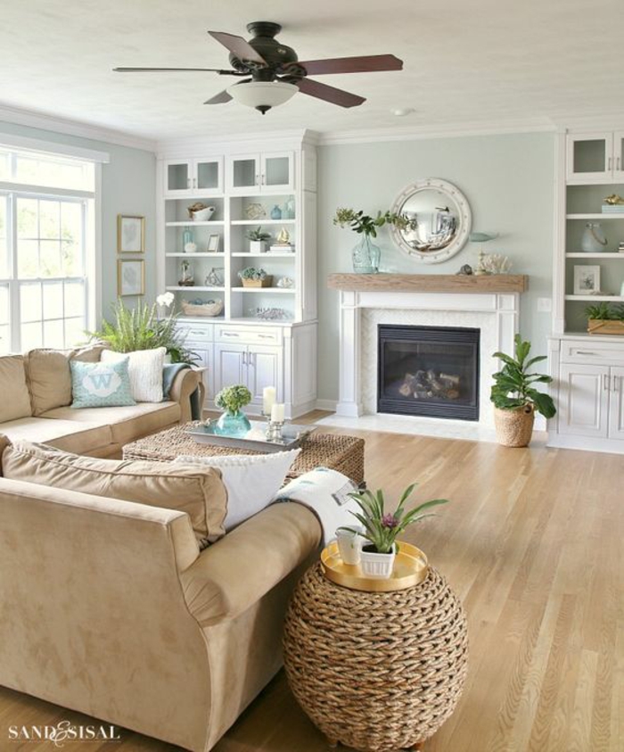 living room paint colors, pale blue walls and white ceiling, lamp with ceiling fan, pale camel-colored sofa, two wicker tables and two white cupboards, fireplace and wooden floors