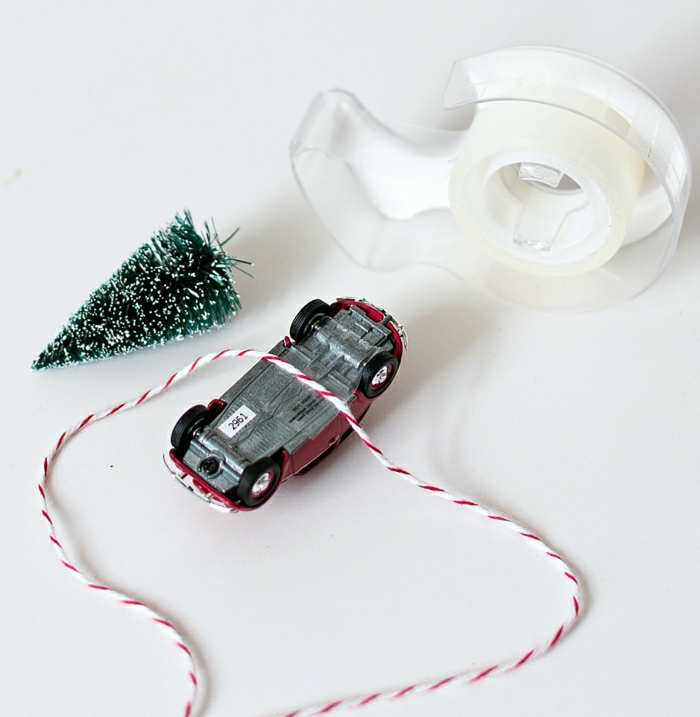 homemade christmas gift ideas, sticky tape on white stand, red car toy turned on its back, a small snowy christmas tree ornament, some white and red string