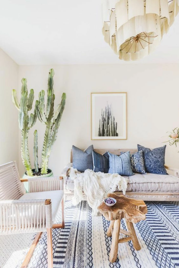 living room color schemes, cream walls and white ceiling, blue and cream carpet, off-white sofa with five blue pillows, white chair with wooden legs, large cactus plant in pot