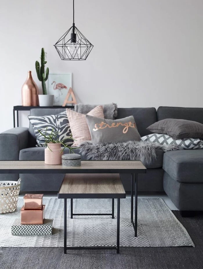 neutral colors, pale grey wall and dark grey sofa with pillows in pink, grey and white, two pale wooden tables with black metal legs, black metal lamp and light grey rug