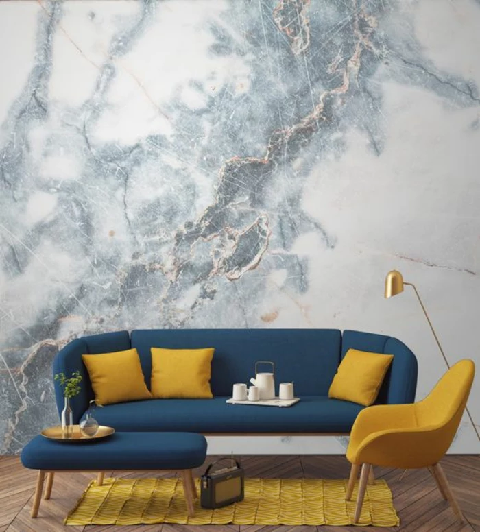 interior painting, marble colored grey and white wallpaper, dark blue sofa with three yellow cushions, yellow chair and rug, dark blue table with gold trey, old radio and wooden floor
