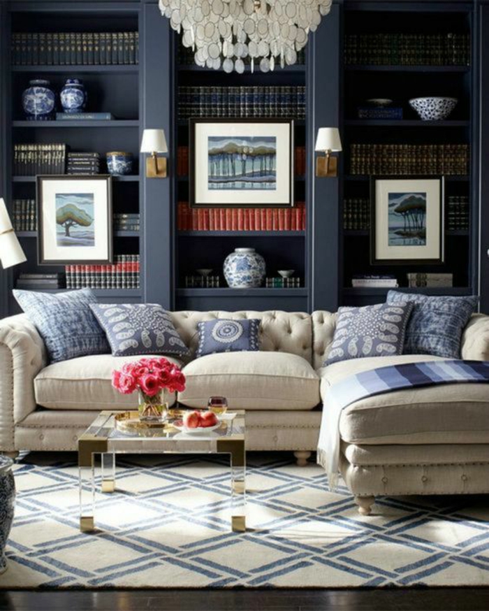 dark blue or black in-built library shelves, light cream sofa with five blue and cream pillows and blanket, small coffee table with flowers and decorations, cream and dark blue carpet