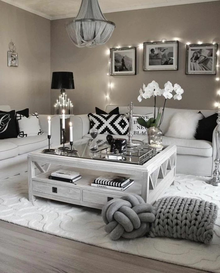 mink-colored walls, two off-white sofas with black and white cushions, white wooden table with glass top, wooden floor and white carpet, three framed images and fairy lights