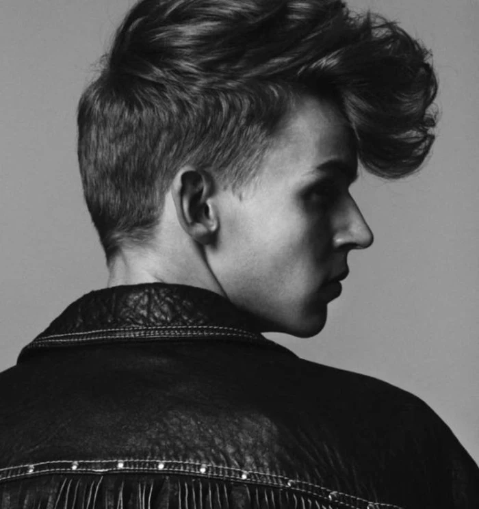 black and white image of young man in profile, leather jacket with studs and tassels, short hair with long gelled up bangs, shadows on face