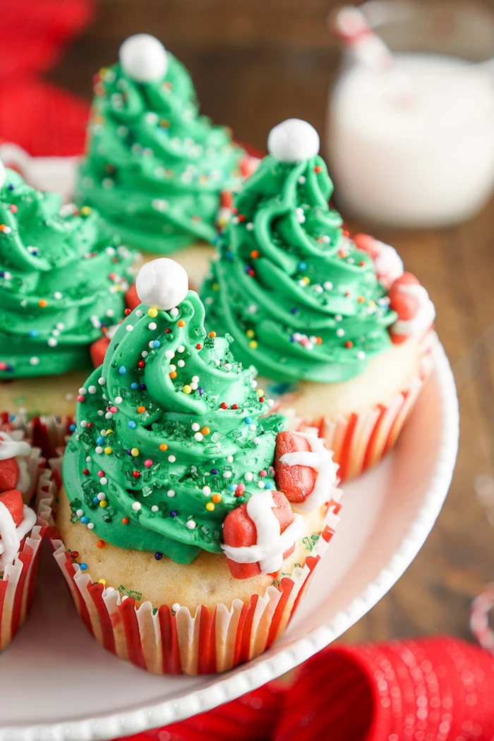 christmas baking ideas, several pale yellow cupcakes, with green frosting made to look like christmas tree, colorful sprinkles white pearls and fondant presents