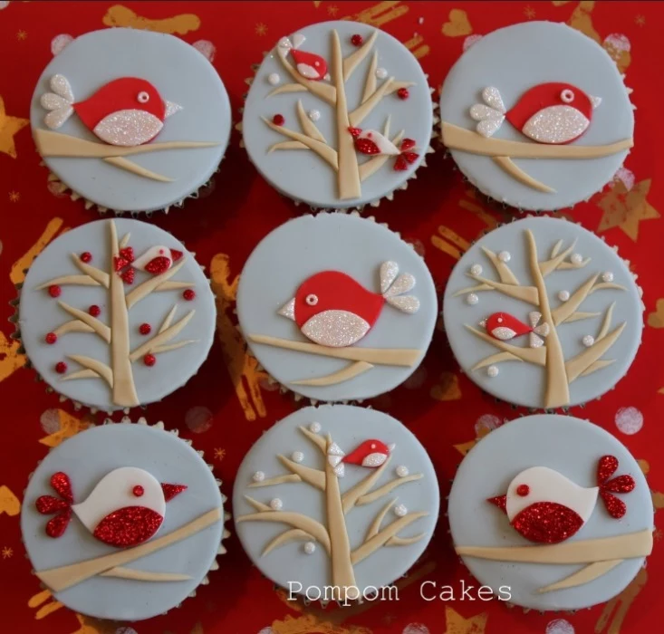 christmas baking ideas, nine cupcakes with pale blue fondant icing, decorated with brown, sparkly red and white fondant birds and trees