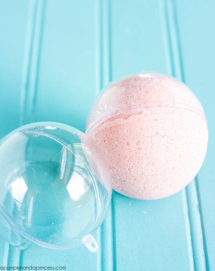 a pale pink bath bomb, in an open clear plastic bauble, on pale blue background