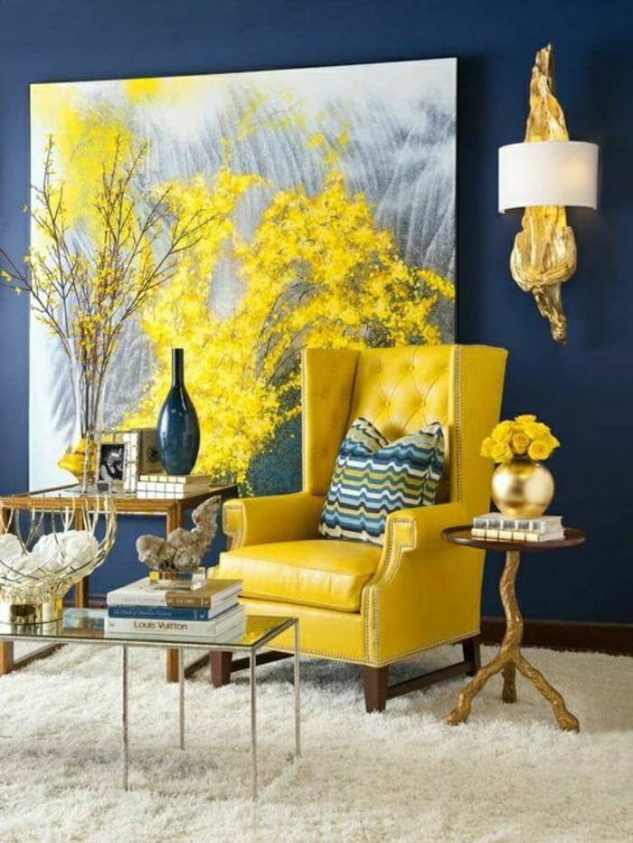 paint colors for living room, fluffy cream carpet, yellow leather chair with green and blue striped cushion, large yellow and grey painting, dark blue wall and gold and white lamp, three different tables