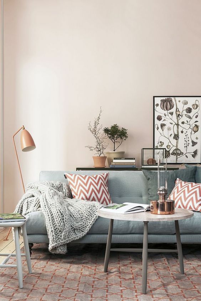 color schemes for living rooms, pale pastel pink wall, pale pastel blue sofa, two dark brownish-red striped cushions, grey chunky knit blanket, pale round coffee table with grey legs