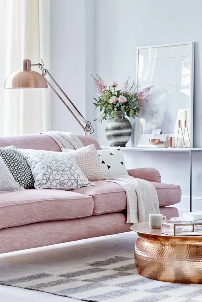 room with pale lilac walls and pale salmon pink sofa, five differently colored cushions, rose gold metal lamp, copper colored round metal table, chequered grey and cream rug