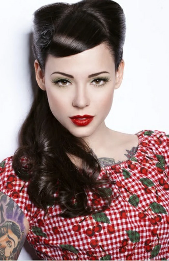 woman dressed and made up in rockabilly style, dark mid-length hair with curls, side bangs and victory rolls, bright red lipstick tattoos and chequered dress with cherry print