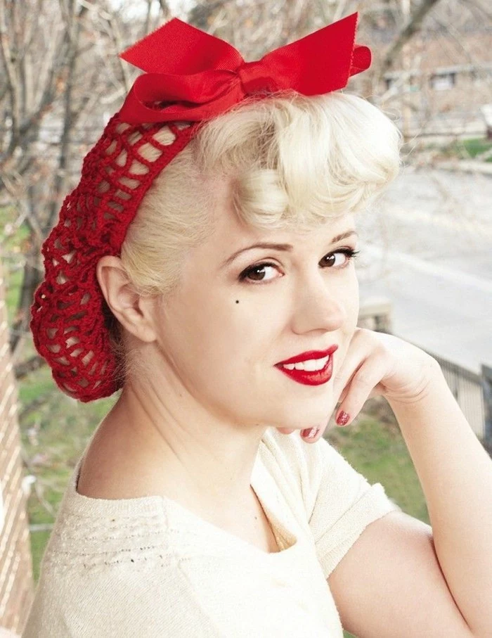 pin up girl hairstyles, woman with black eyes, strong red lipstick and a beauty spot, platinum hair gathered in a red hair net with a bow, curly bangs and white teeth