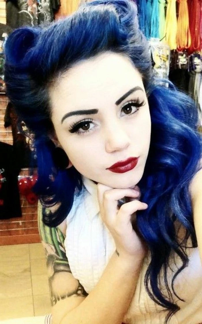 blue-haired pale girl with dark red lipstick and heavy eye make up, fake lashes eyeliner mascara penciled eyebrows, tattoo on arm and white top